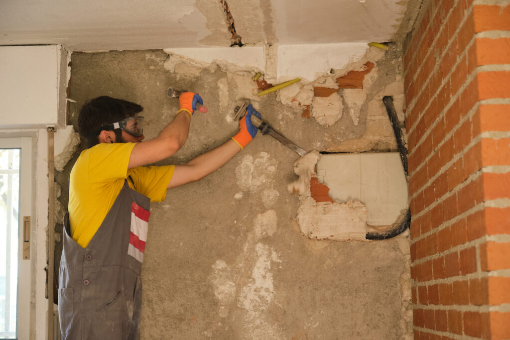 Young caucasian construction worker breaking up a house wall with a hammer and a chisel. Young builder breaking up a house wall with a hammer and a chisel.